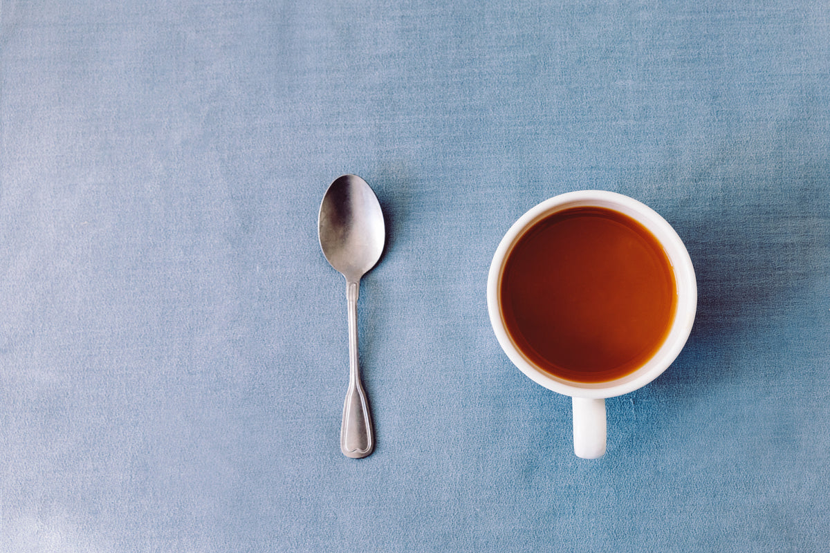 Cup of tea and spoon on linen blue tablecloth seen from above